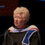 A woman in graduation gown speaking at an event.